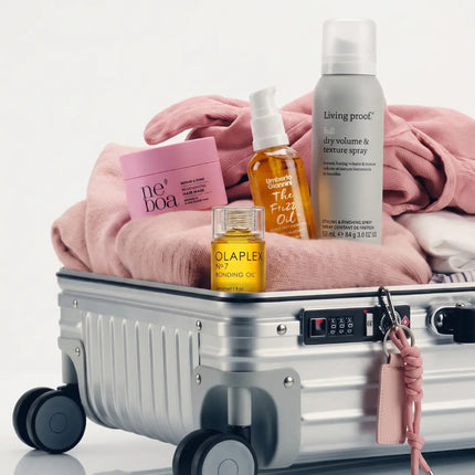 Haarverzorging in reisformaat op een handbagagekoffer: haarolie, droogshampoo, een haarmasker en textuurspray